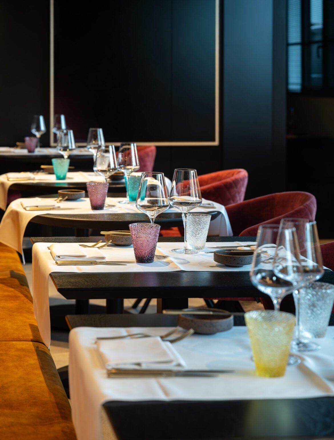 Rows of tables set with colorful glassware and stemware, black table tops, folded napkins, minimal tableware,