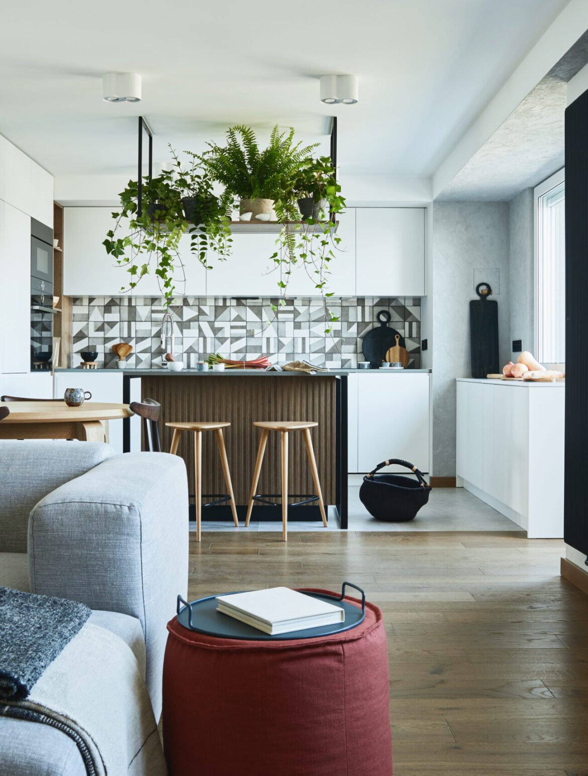 Stylish living room interior design with grey sofa, pouf and personal accessories. Dining space and kitchen on the background. Creative walls with woode pannels. Minimalistic style an plant love concept.