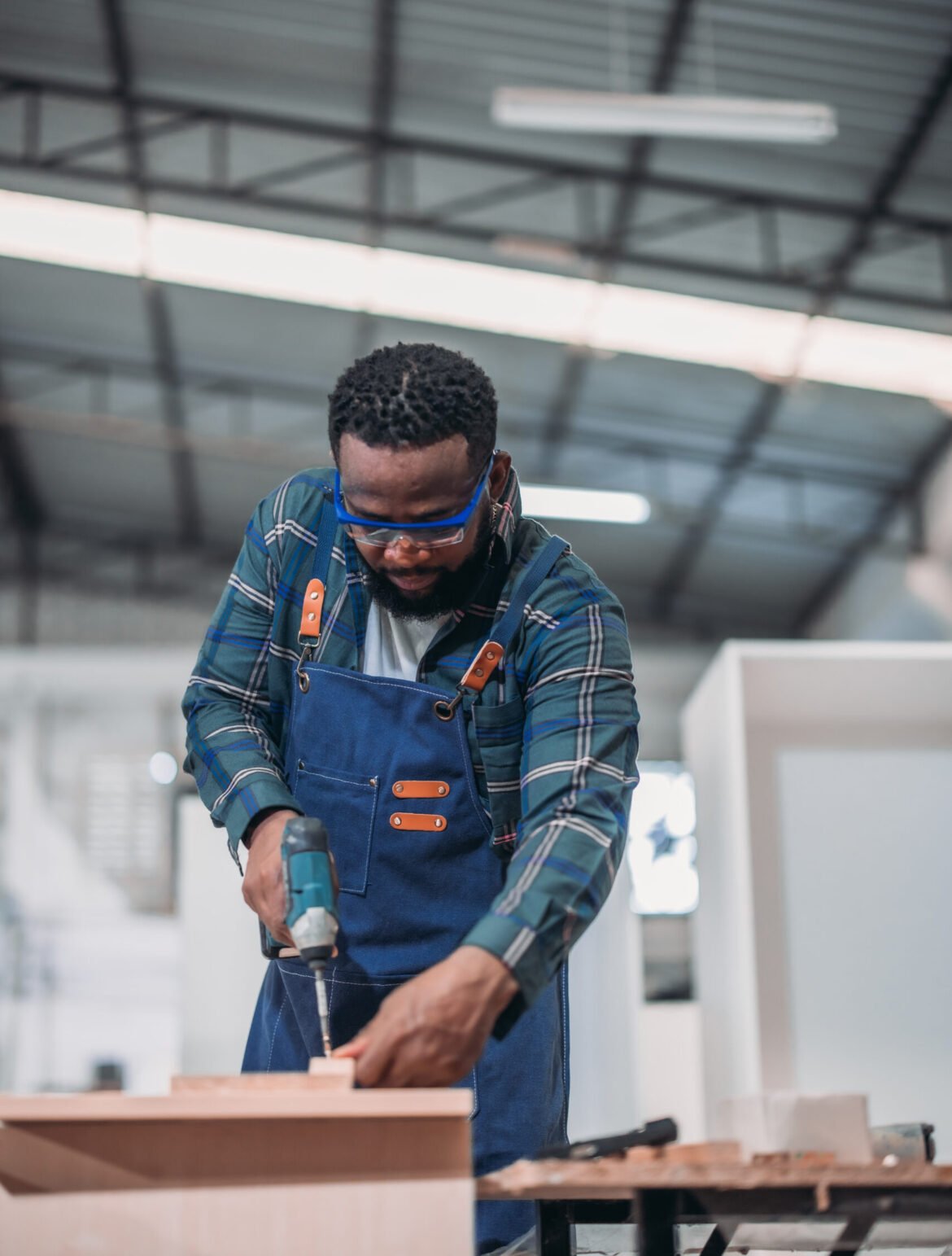 The carpenter uses a power drill to make accurate holes in the wood, skillfully creating the furniture product with experienced precision.